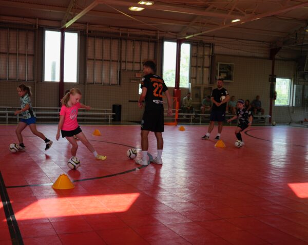Young players dribbling through cones on a red futsal court